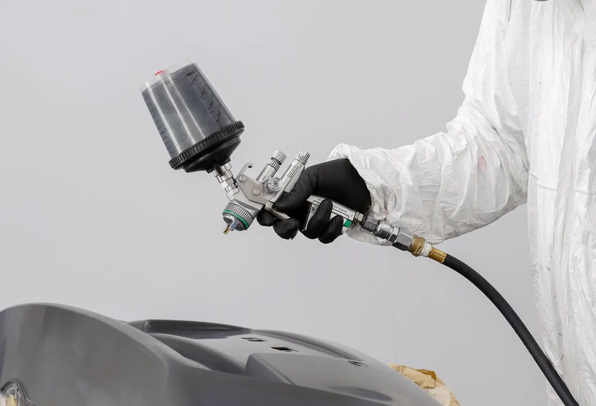 Pintor com pistola de pintura aplicando tinta em peça de carro