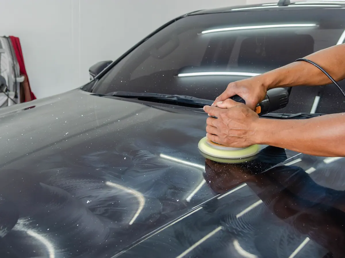 Mãos usando politriz no capô de um carro preto